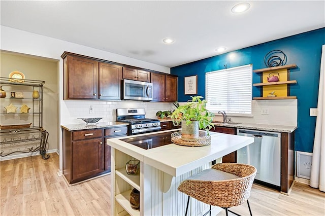 kitchen featuring light wood finished floors, open shelves, appliances with stainless steel finishes, and a sink