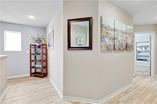 hall with light wood-type flooring, visible vents, and baseboards