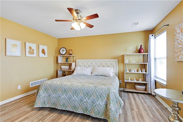 bedroom featuring a ceiling fan, visible vents, baseboards, and wood finished floors