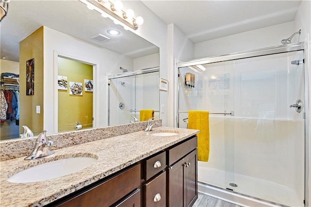 bathroom featuring visible vents, a sink, a shower stall, and double vanity