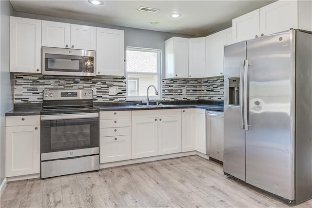 kitchen featuring sink, stainless steel appliances, light hardwood / wood-style floors, decorative backsplash, and white cabinets