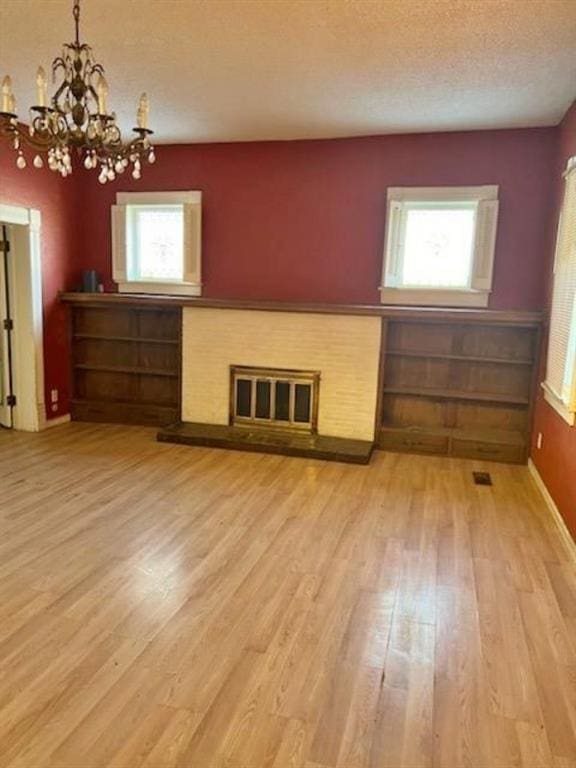 unfurnished living room featuring a notable chandelier, a textured ceiling, and light wood-type flooring