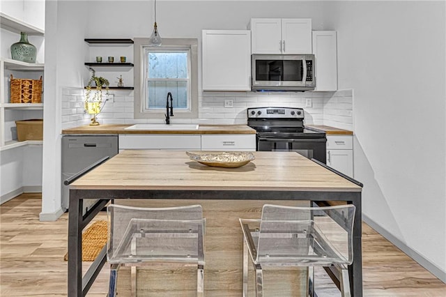 kitchen with stainless steel appliances, pendant lighting, white cabinets, and light wood-type flooring