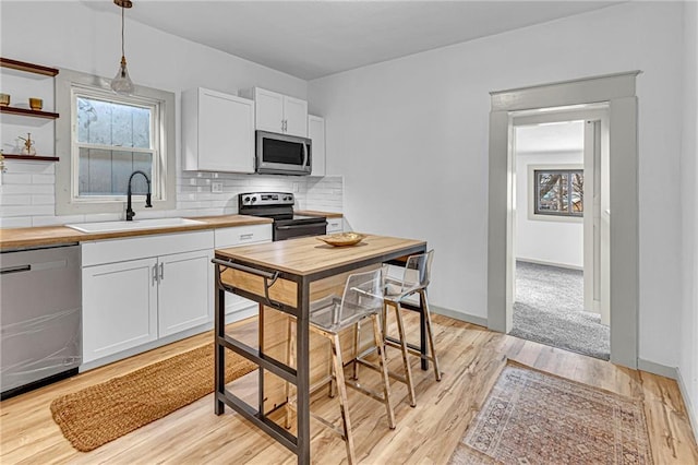 kitchen featuring appliances with stainless steel finishes, pendant lighting, sink, white cabinets, and decorative backsplash