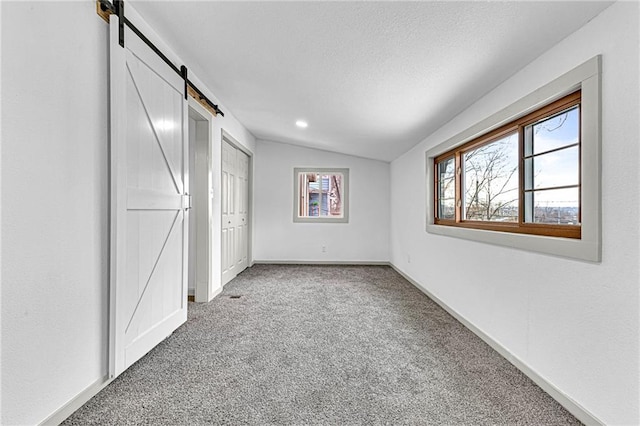 unfurnished bedroom with vaulted ceiling, a barn door, carpet, and a textured ceiling