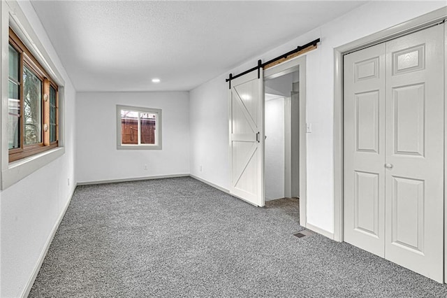 unfurnished bedroom with vaulted ceiling, a barn door, carpet floors, and a closet