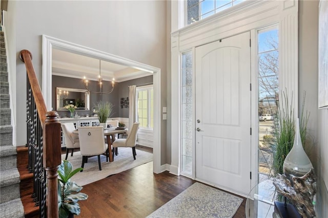 foyer entrance featuring crown molding, a notable chandelier, dark wood finished floors, a raised ceiling, and stairway