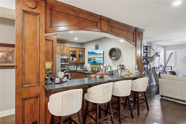 kitchen featuring a peninsula, appliances with stainless steel finishes, dark countertops, and brown cabinets