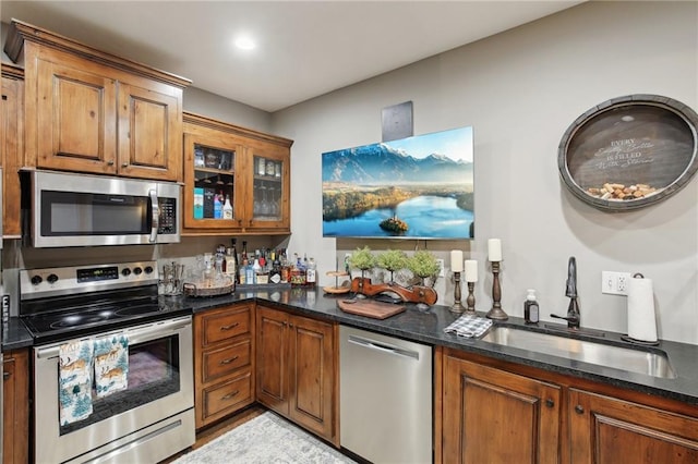 kitchen with stainless steel appliances, dark stone counters, brown cabinets, and a sink