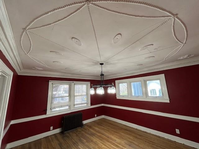 spare room with ornamental molding, baseboards, radiator heating unit, and wood finished floors