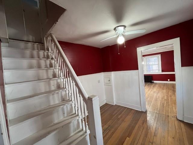 stairs with a wainscoted wall, radiator heating unit, ceiling fan, and hardwood / wood-style floors