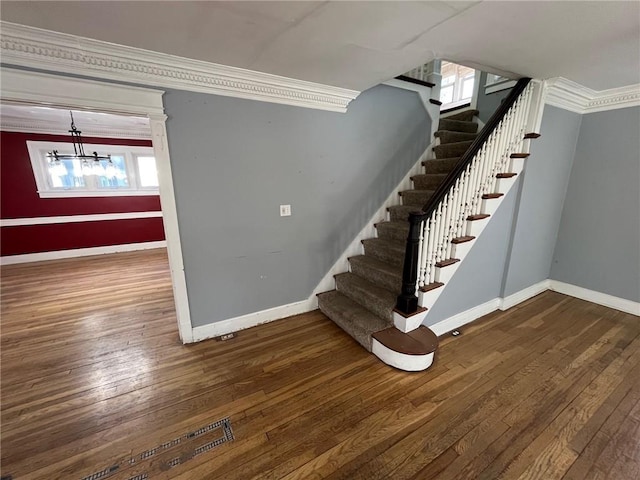 stairway with an inviting chandelier, crown molding, baseboards, and hardwood / wood-style flooring