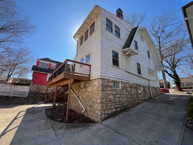 view of property exterior featuring stairway, a chimney, a wooden deck, and fence