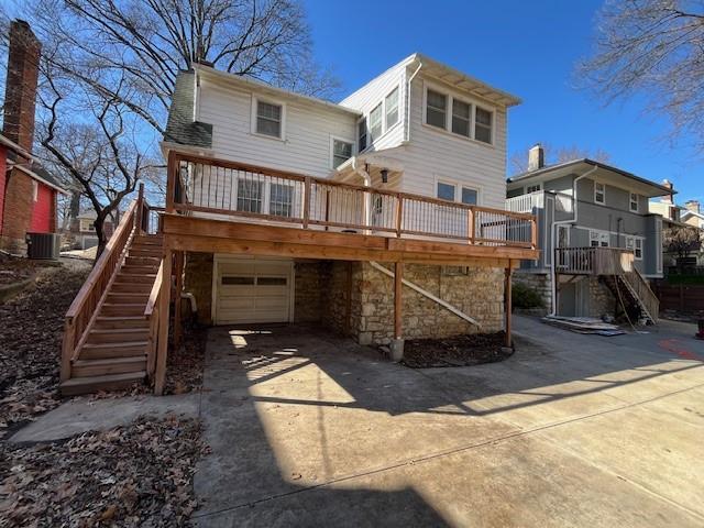 rear view of property featuring concrete driveway, a garage, stone siding, a wooden deck, and stairs