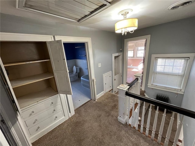 hallway featuring carpet floors, baseboards, visible vents, and an upstairs landing