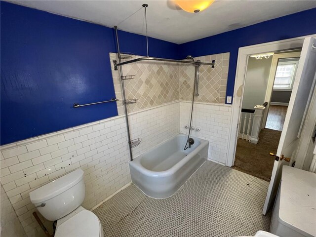 full bathroom featuring a wainscoted wall, tile walls, toilet, and bathing tub / shower combination