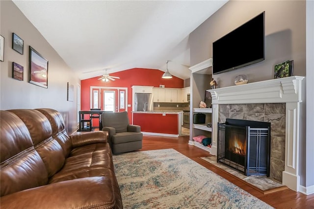 living area featuring lofted ceiling, a tiled fireplace, wood finished floors, and a ceiling fan