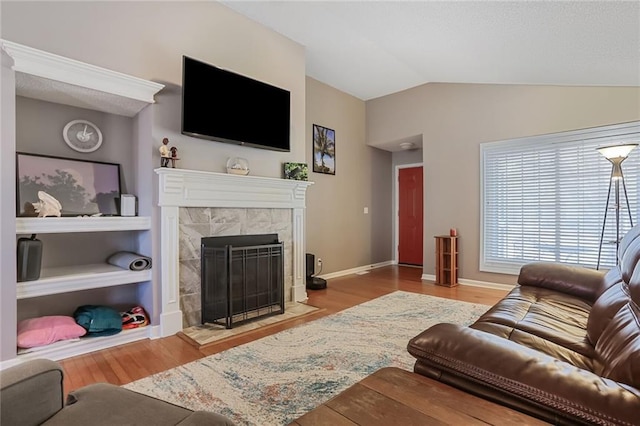 living area featuring baseboards, vaulted ceiling, a tiled fireplace, and wood finished floors