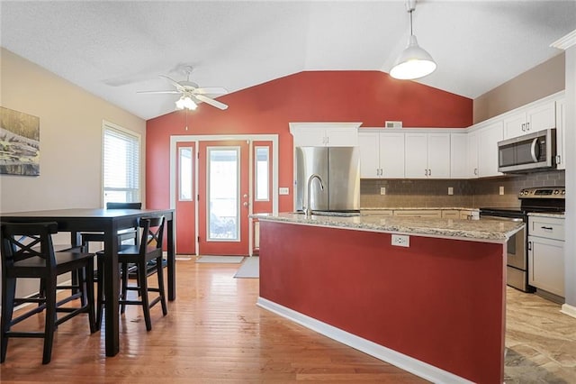 kitchen featuring appliances with stainless steel finishes, white cabinetry, backsplash, and an island with sink