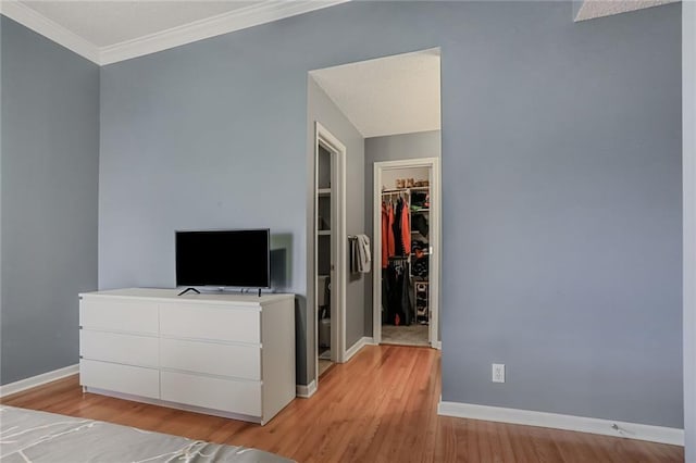 unfurnished bedroom with baseboards, a walk in closet, crown molding, light wood-type flooring, and a closet