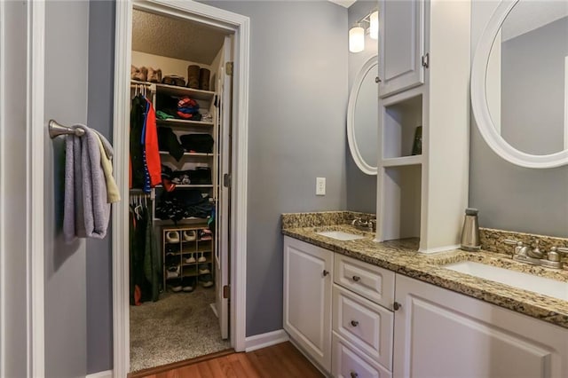 full bathroom with double vanity, a spacious closet, a sink, and wood finished floors