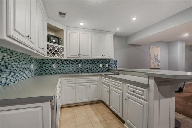 kitchen featuring light tile patterned floors, a peninsula, a sink, visible vents, and white cabinetry