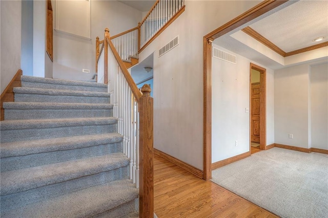 stairs featuring hardwood / wood-style flooring, ornamental molding, and a raised ceiling