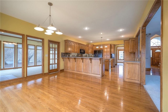 kitchen with light hardwood / wood-style floors, black appliances, decorative backsplash, decorative light fixtures, and kitchen peninsula