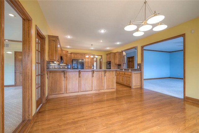 kitchen featuring pendant lighting, kitchen peninsula, light hardwood / wood-style floors, and black appliances