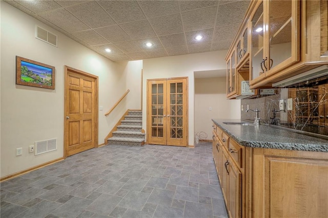 kitchen featuring sink, dark stone countertops, a drop ceiling, decorative backsplash, and french doors