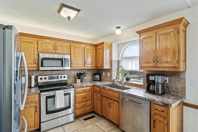 kitchen with sink, light tile patterned floors, stainless steel appliances, a textured ceiling, and decorative backsplash