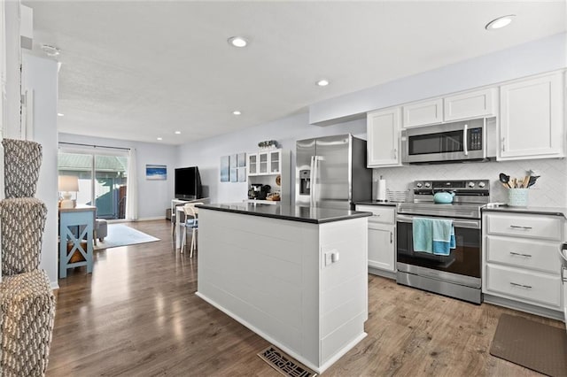 kitchen with appliances with stainless steel finishes, backsplash, wood finished floors, and white cabinetry