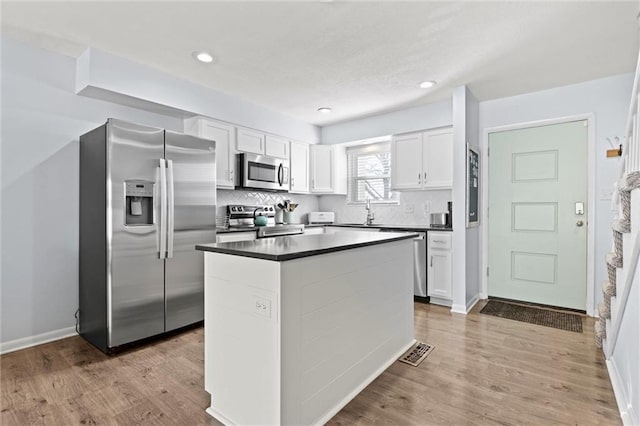 kitchen with appliances with stainless steel finishes, dark countertops, white cabinetry, and tasteful backsplash