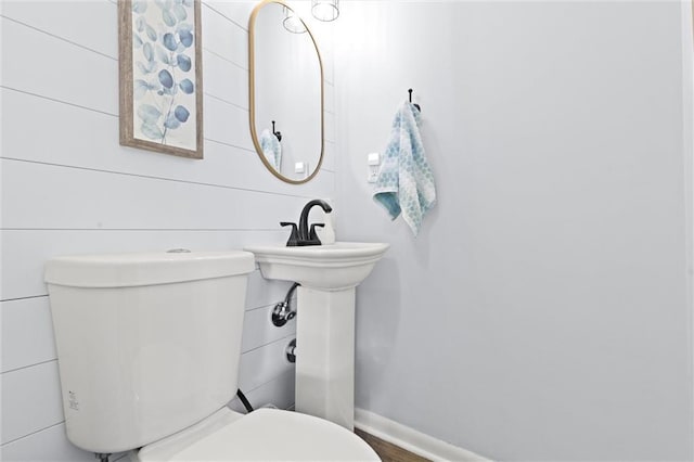 half bath featuring baseboards and toilet