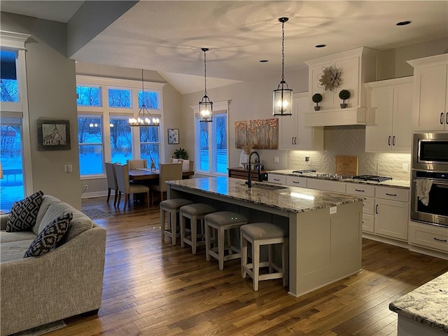 kitchen with sink, decorative light fixtures, stainless steel appliances, a kitchen island with sink, and white cabinets