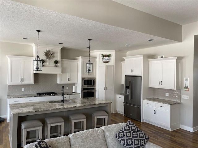 kitchen with stainless steel appliances, a kitchen breakfast bar, decorative light fixtures, and an island with sink