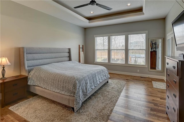 bedroom featuring crown molding, light hardwood / wood-style flooring, ceiling fan, and a tray ceiling