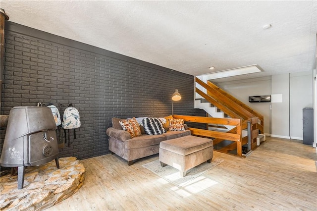 living area with brick wall, stairway, light wood-style flooring, and baseboards