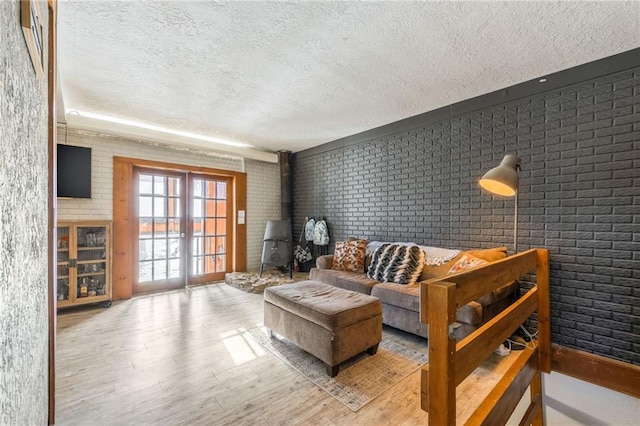 living room featuring a wood stove, light wood finished floors, brick wall, and a textured ceiling