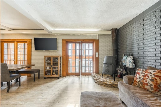 living room featuring beam ceiling, a wood stove, a textured ceiling, brick wall, and wood finished floors