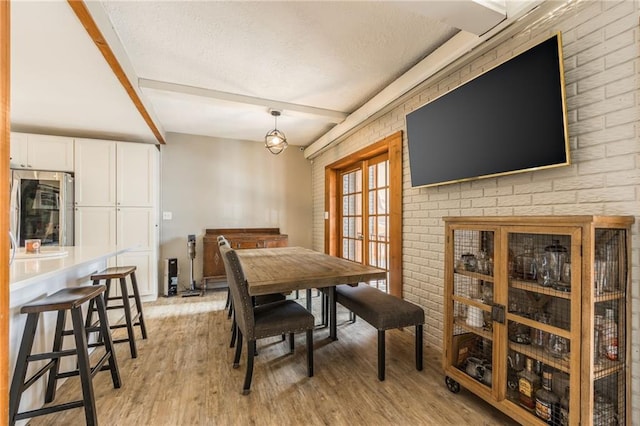 dining space featuring a textured ceiling, light wood-type flooring, and beam ceiling