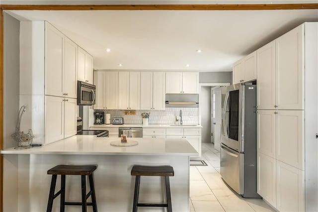 kitchen with a breakfast bar area, white cabinetry, light countertops, appliances with stainless steel finishes, and tasteful backsplash