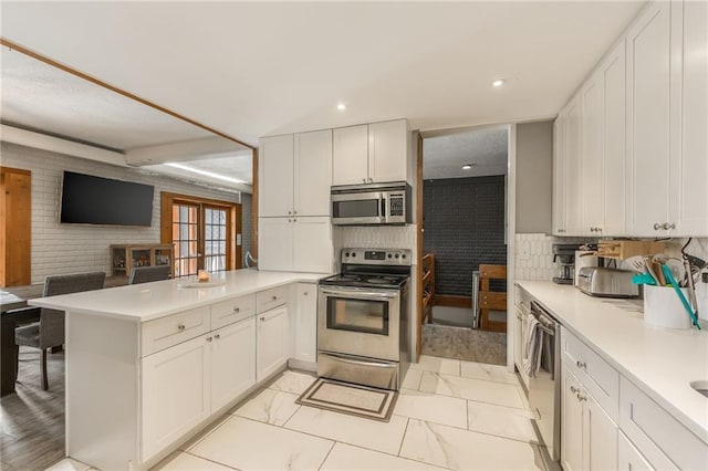 kitchen with appliances with stainless steel finishes, marble finish floor, light countertops, and a peninsula