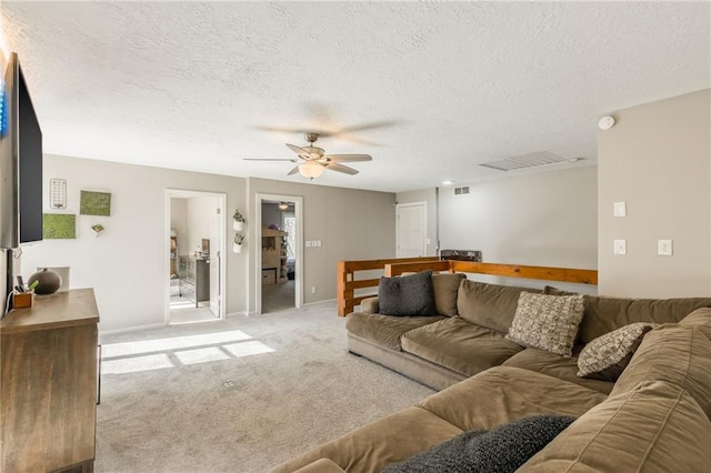 living room featuring light colored carpet, visible vents, ceiling fan, a textured ceiling, and baseboards