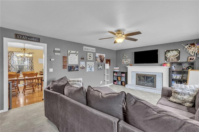 living room with light wood-type flooring, ceiling fan with notable chandelier, and a fireplace