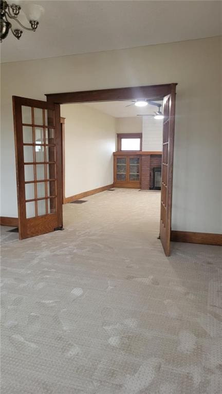 spare room with light colored carpet and a brick fireplace