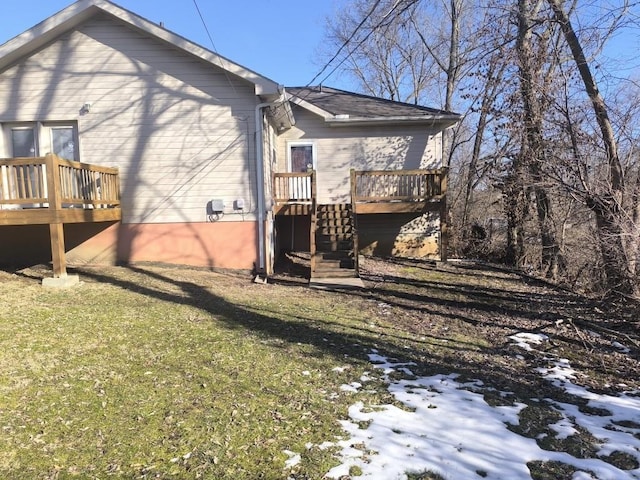 snow covered rear of property featuring a wooden deck and a yard