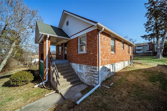 view of front facade featuring brick siding, roof with shingles, and a front yard