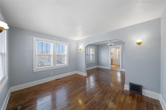 unfurnished room with arched walkways, visible vents, dark wood finished floors, and baseboards