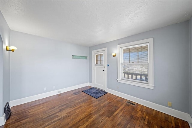 foyer entrance with baseboards, visible vents, dark wood finished floors, and a textured ceiling